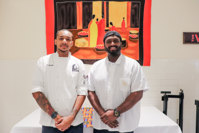 Sous-chef Ray Sharp (left) and cook Morgan Townsend (right) posing in front of a banner honoring African heritage.