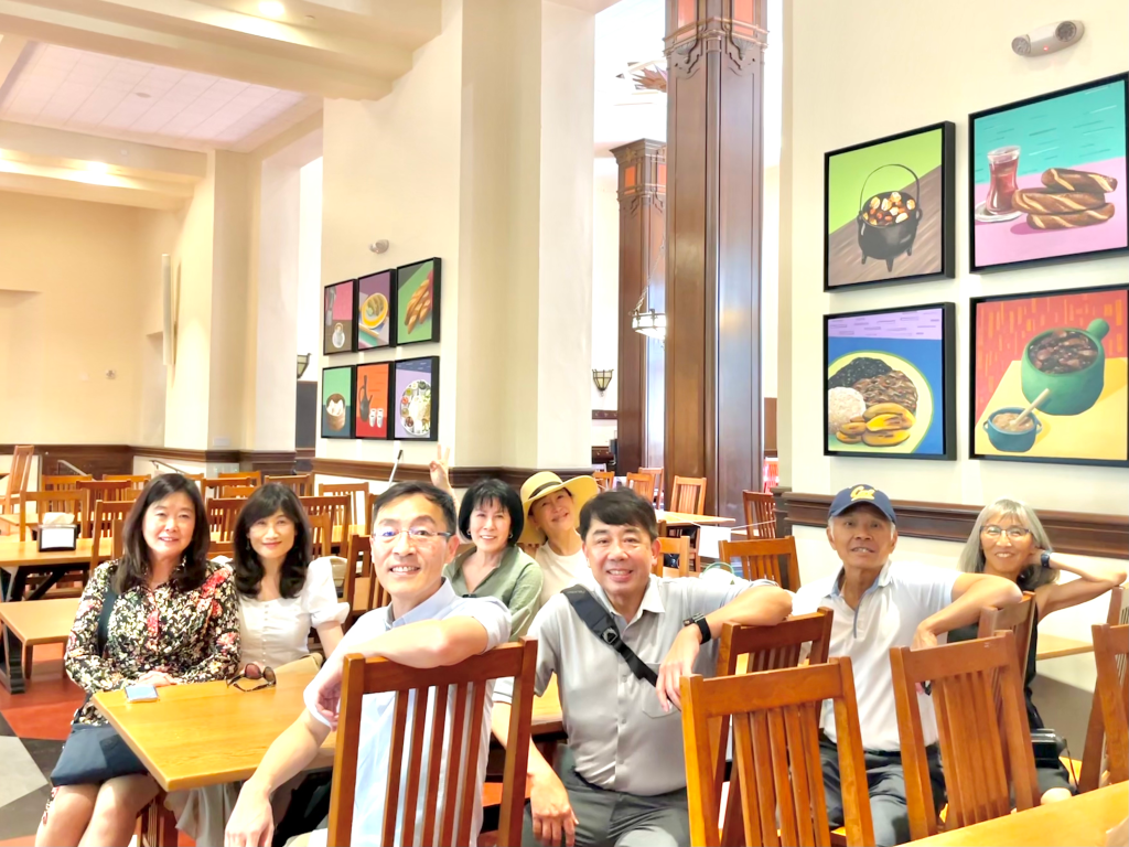 Group of 8 alumni sitting at big table in dining hall