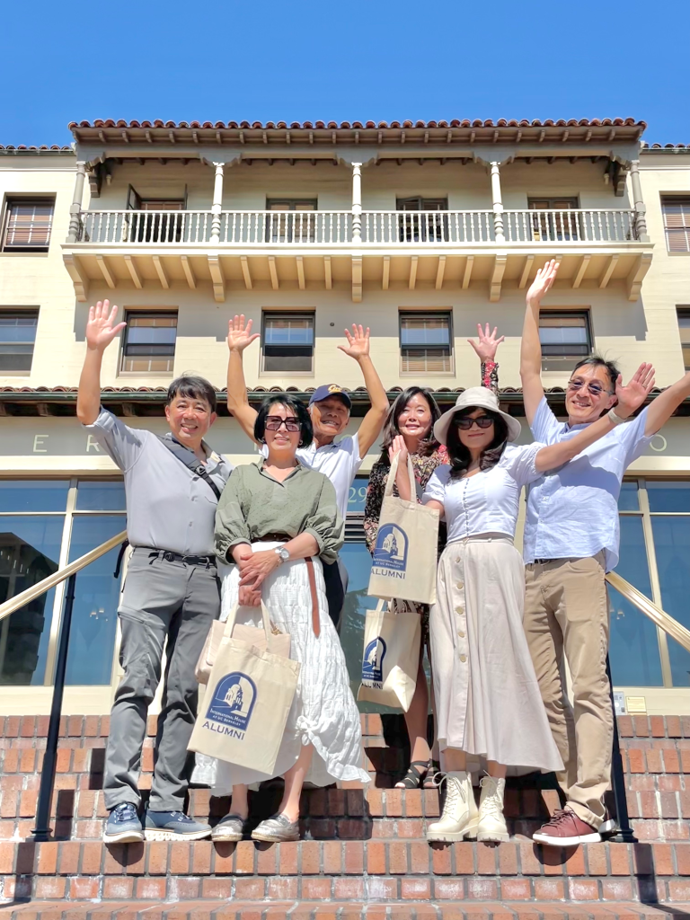 Alumni on front steps waving and smiling, from left: Jimmy Lo (in grey pants), Daisy Loh (in green shirt), Howard Leung (with a Cal cap), Judy Chu (in a floral dress), Louisa Ho (with white hat), John Hwa (in khaki pants). 
