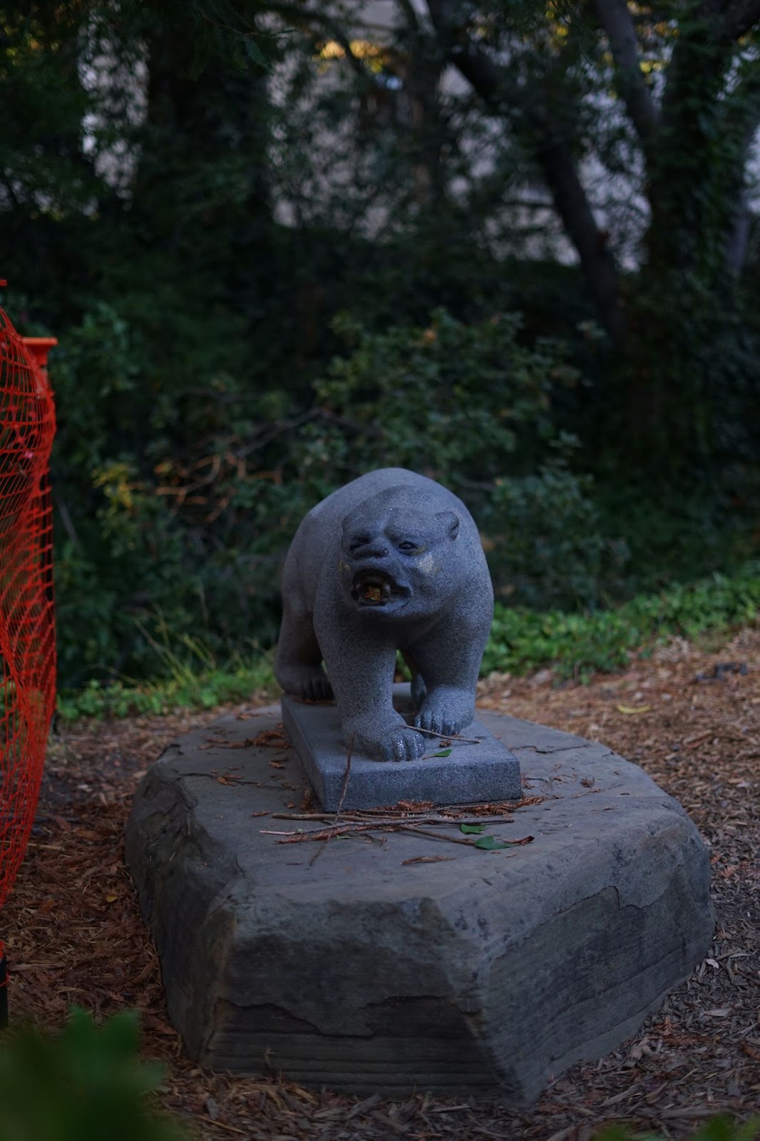 A statue of a bear walking, with trees and a creek in the background.