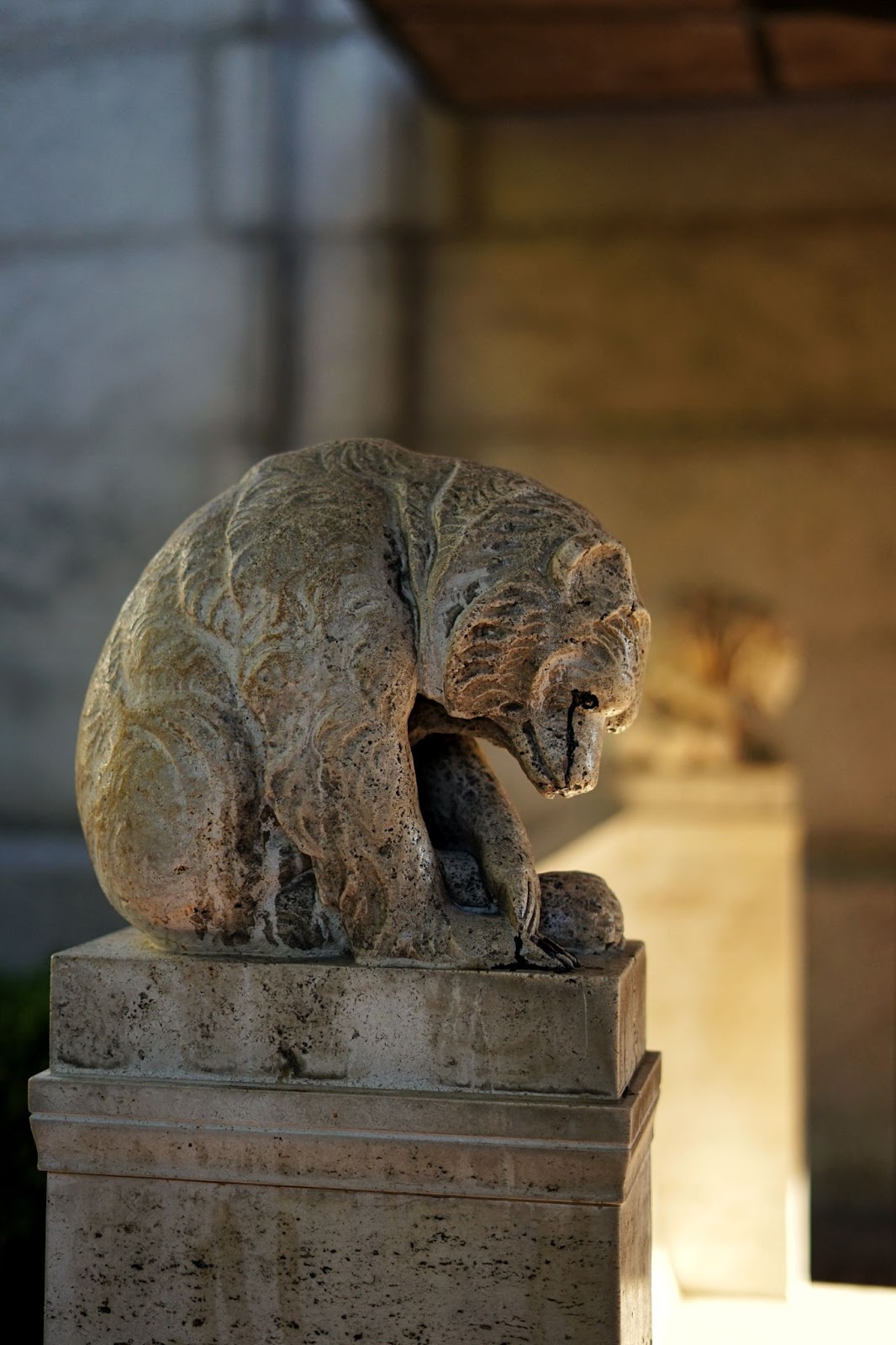 A bear statue on the left end of a bench. 