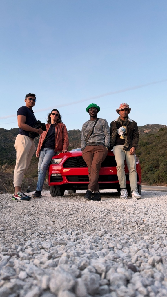 Four people posing in front of a red sports car.