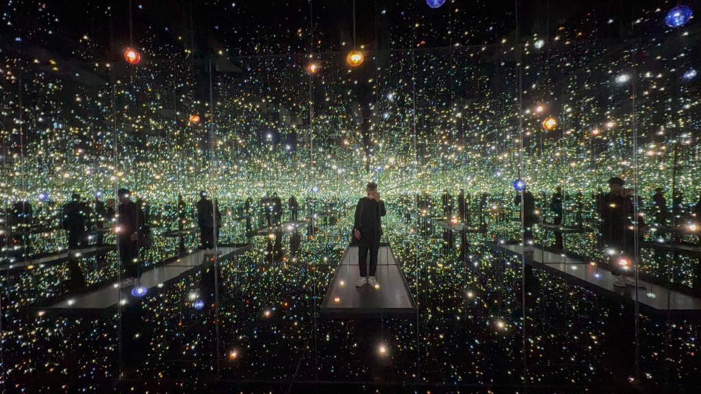 Mirror selfie of a man in a hall of mirrors with lights reflecting.