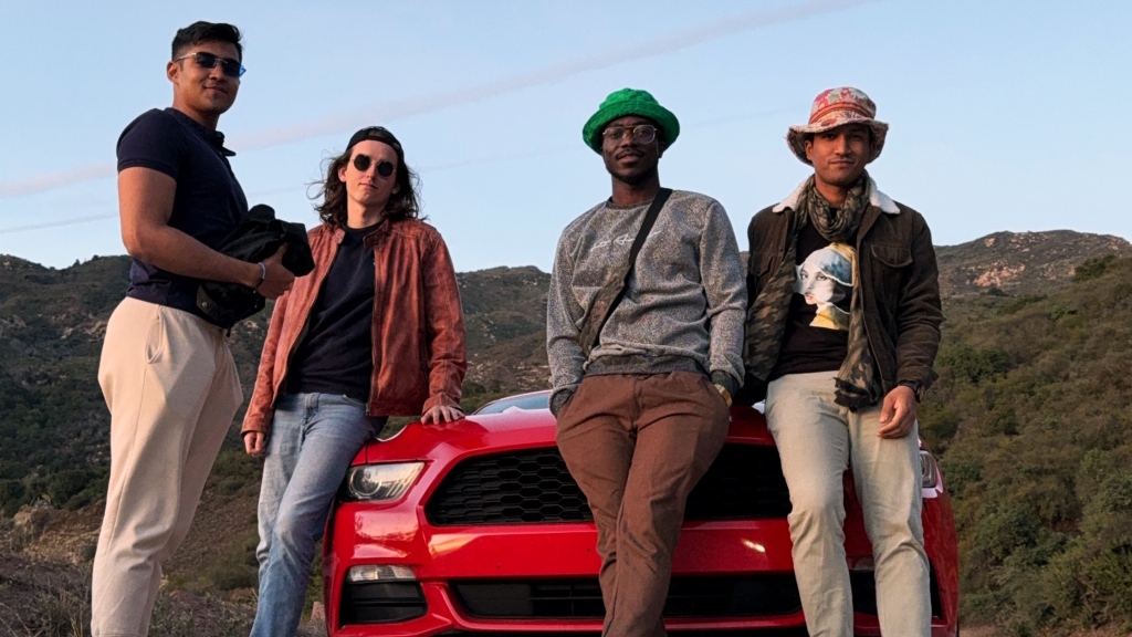 Four I-House residents posing in front of a red sports car.