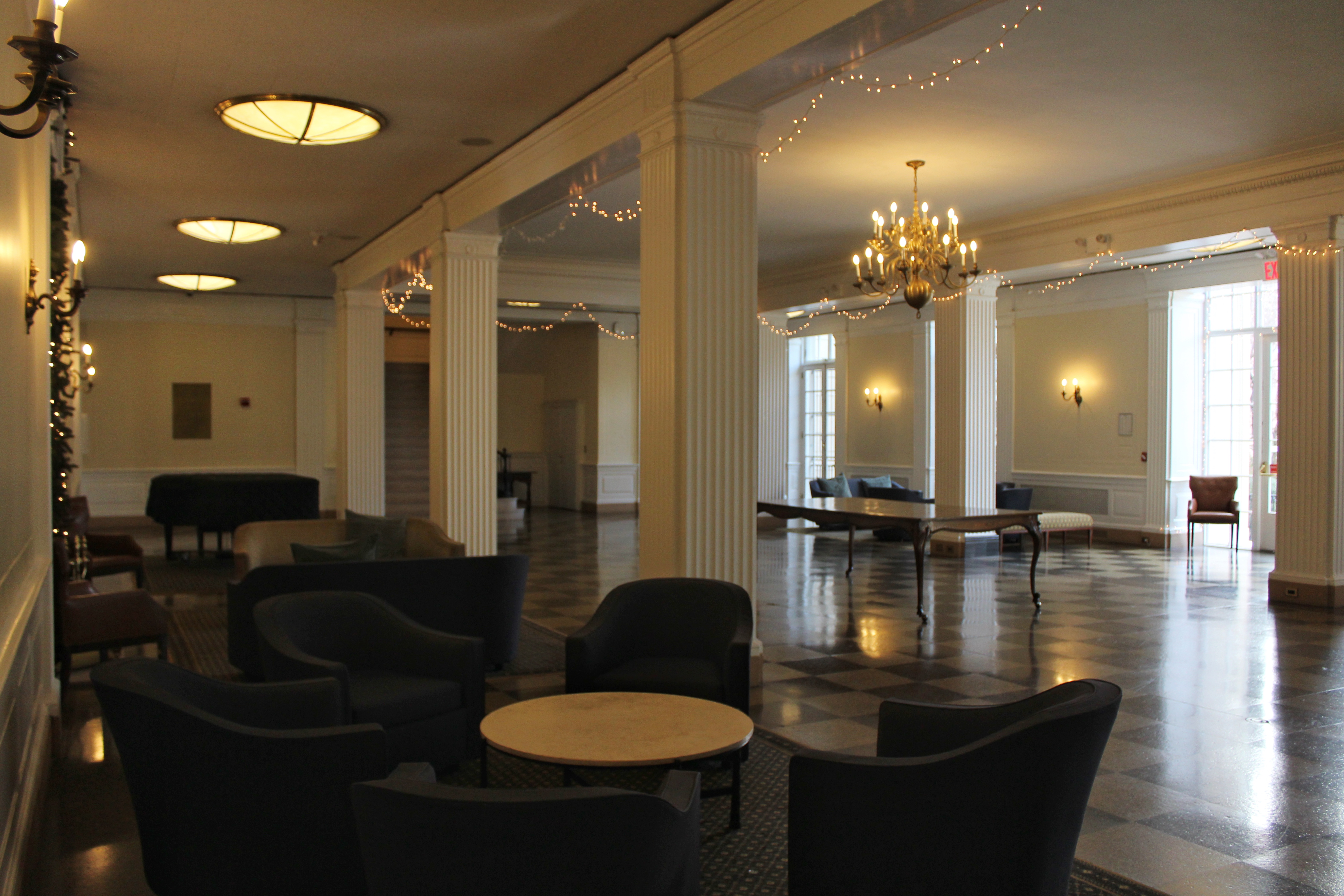 Armchairs around a round table inside a lobby with many lighting fixtures.