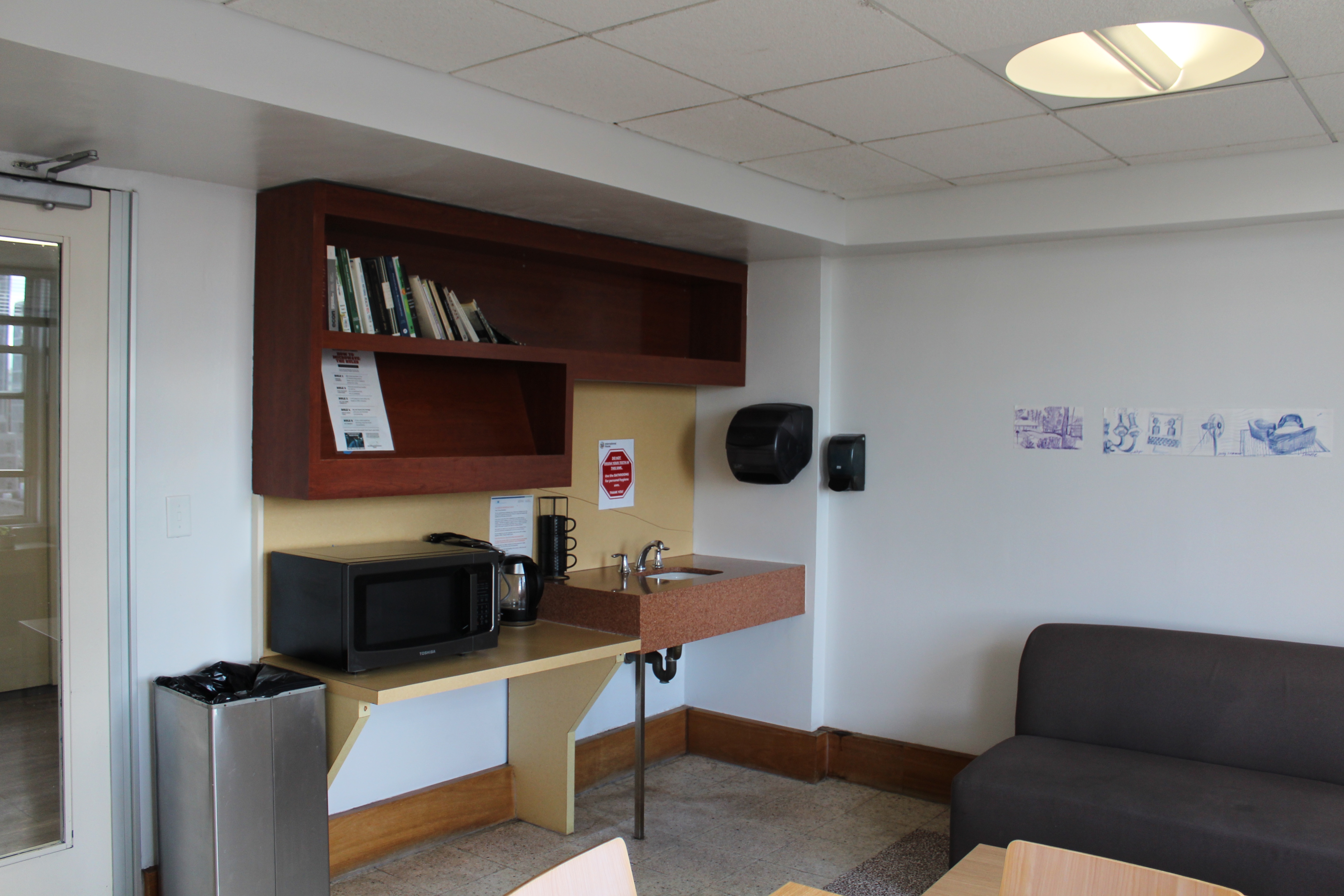 A common room seating area with shelves, a sink, a microwave and a sofa.